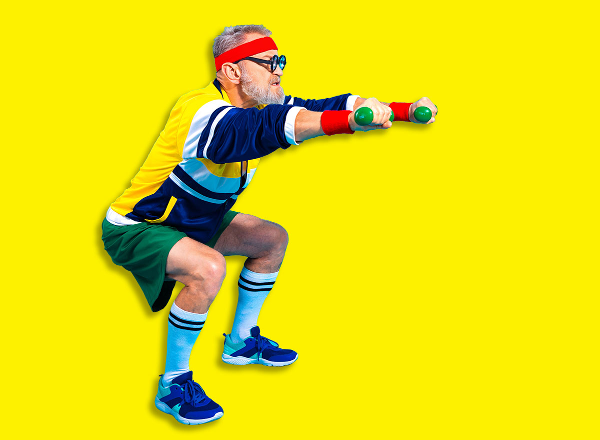 Energetic older man in retro sportswear squats while holding small dumbbells, conveying fitness, active aging, strength and playful style against a vibrant blue backdrop.