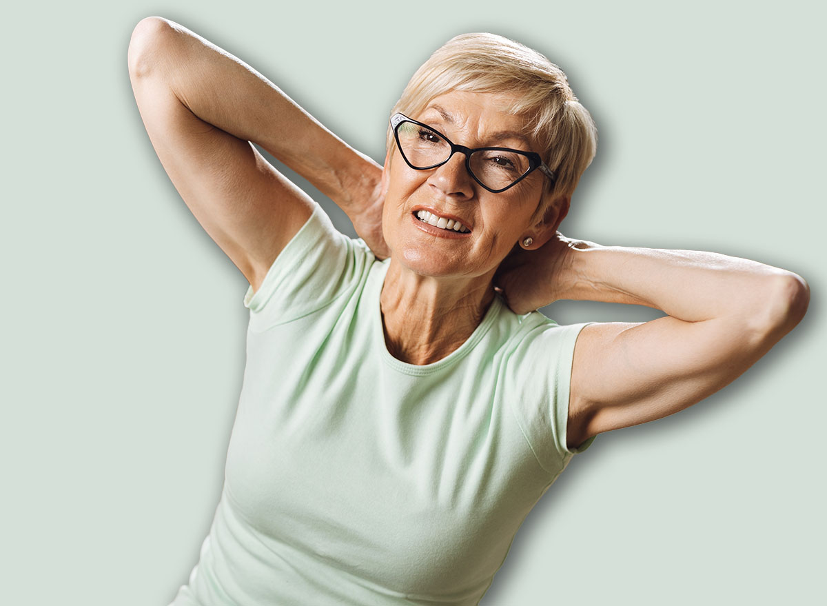 Smiling senior woman doing sit-ups with hands behind her head in the living room
