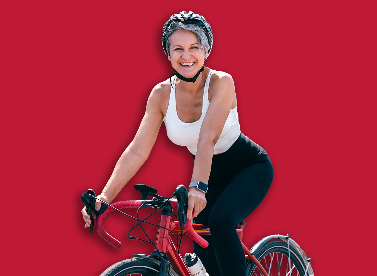 Happy sporty woman in helmet and white top cycling in park and smiling at camera