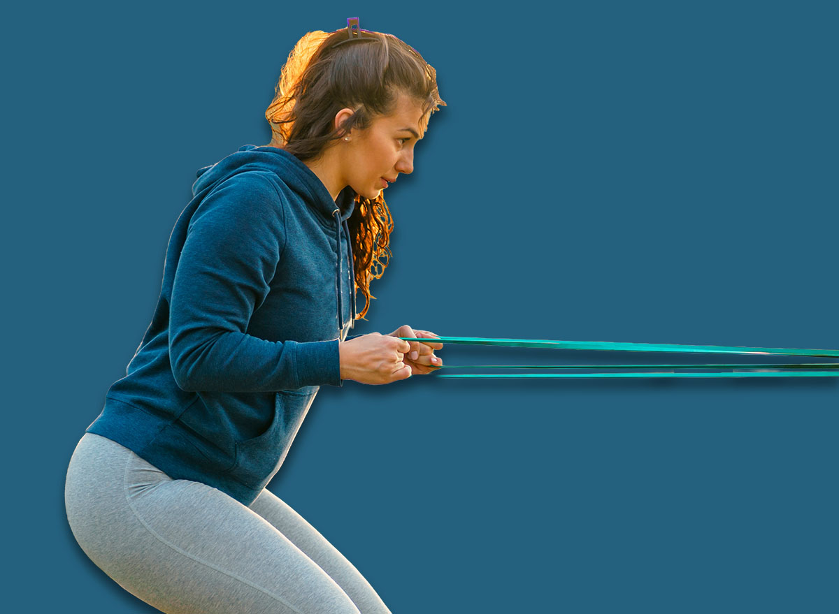 A smiling woman with curves exercises in the park with resistance bands.