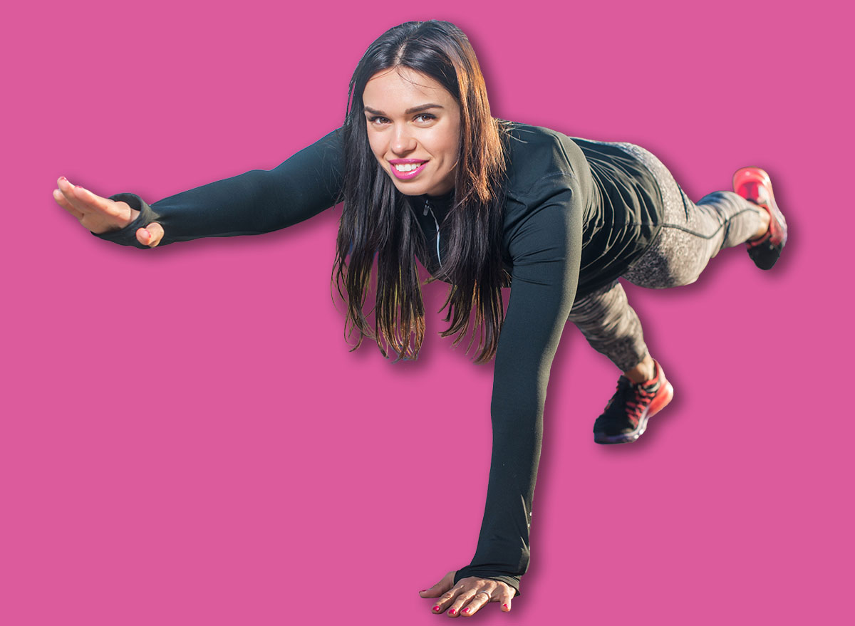 Fit woman doing raised leg plank yoga pilates exercises training her abs core muscles outdoors looking at camera