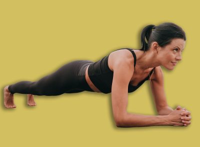 Woman holds a forearm plank on the mat, eyes forward, as the ocean provides a calm yet powerful backdrop for her workout.