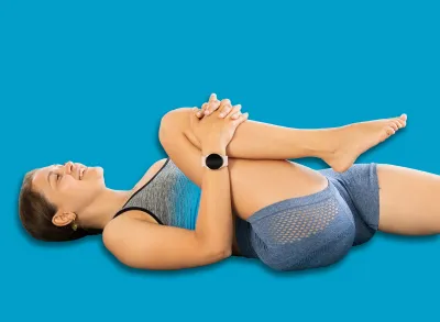 Sportive young girl practicing knee to chest pose of yoga on blue mat in light room