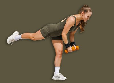Woman performs a single leg dumbbell deadlift outdoors on a mat in a bright garden, showcasing strength, balance and core stability for wellness content.