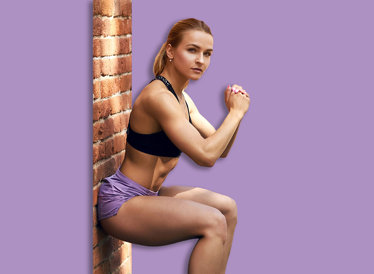 young beautiful woman with ponytail in stylish top and shorts performing squats, full length side view photo. copy space. wellness, wellbeing