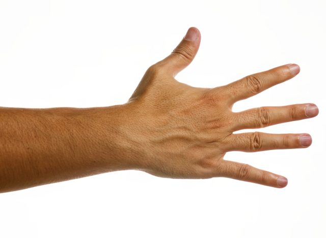 Man's hand with fingers spread apart isolated over white wall background