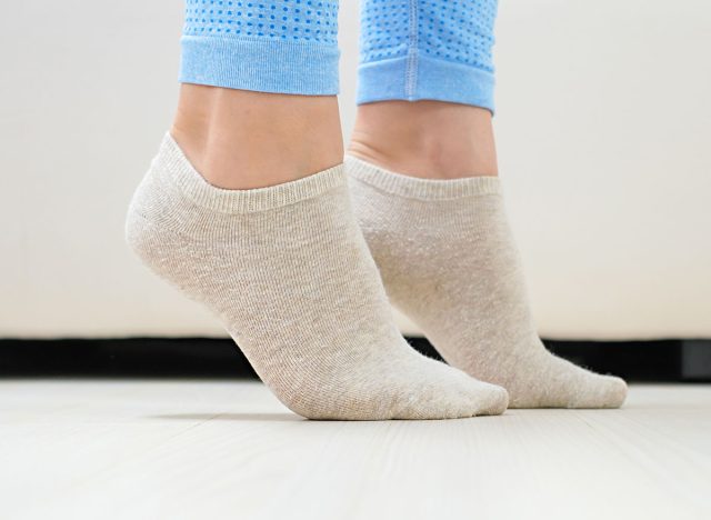 Female legs doing exercises lifting on toes close-up, home workout concept.