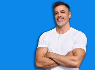 Happy fit sporty older man coach, middle aged sportsman athlete or personal trainer wearing white t-shirt showing muscles standing isolated on gray background advertising gym membership. Portrait.