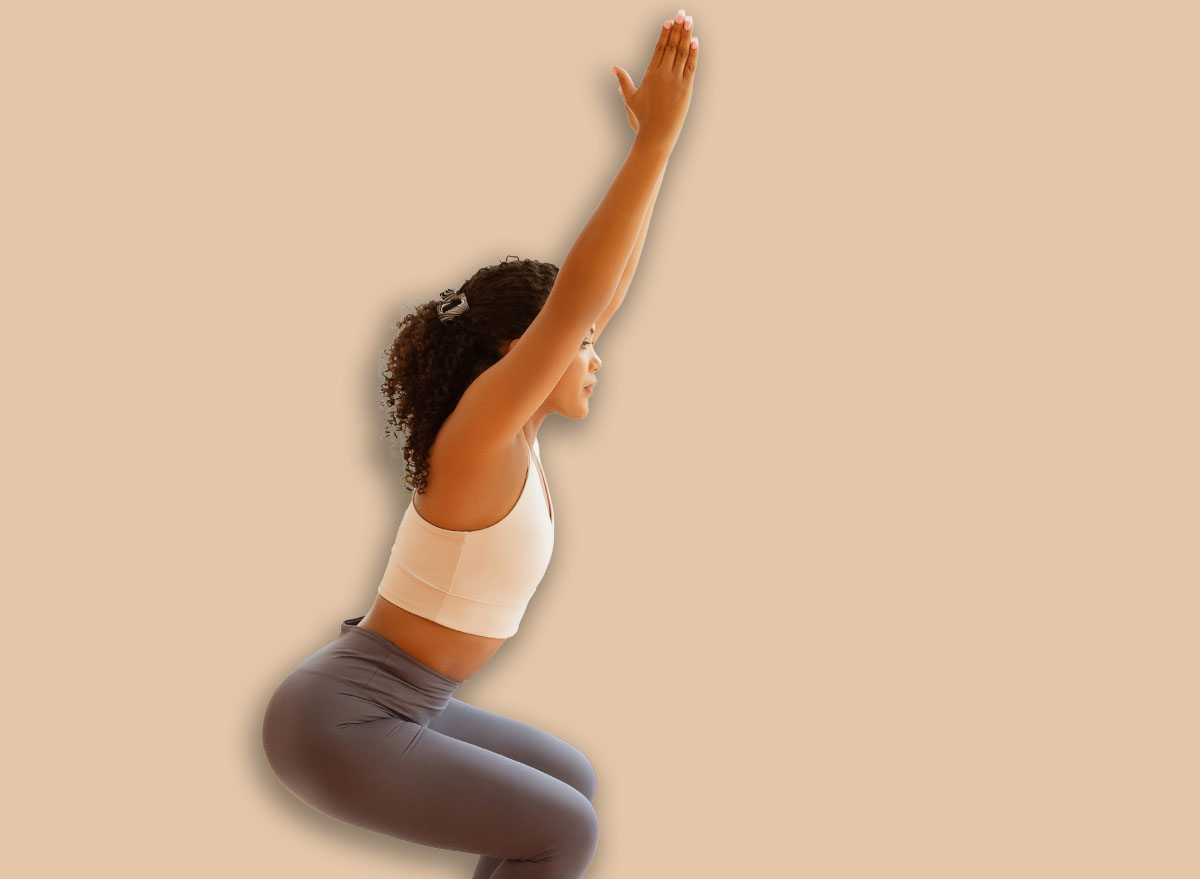 Young lady doing squats with raised arms indoors, engages in domestic workout routine, strengthening her muscles with aerobics and pilates exercises in her living room interior