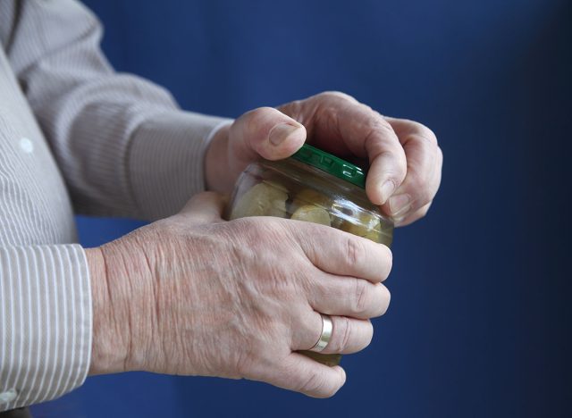 an older man struggles to open a jar of pickles