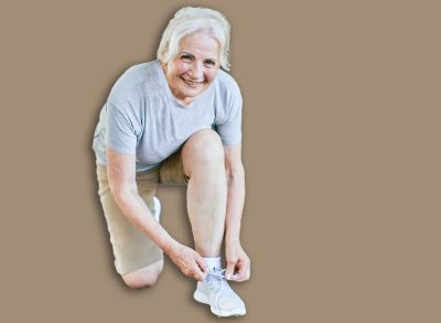 Portrait of a happy active beautiful senior woman posing fixing shoelace on her running shoe after exercising outdoors