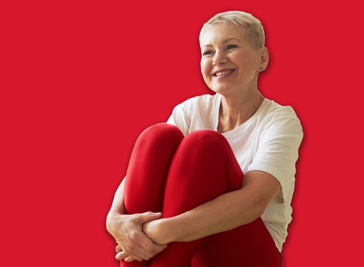 Active lifestyle, wellbeing and age concept. Happy energetic middle aged woman instructor sitting on green mat embracing knees and smiling showing asanas during yoga class in spacious room
