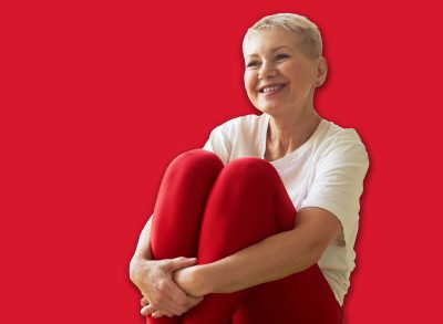 Active lifestyle, wellbeing and age concept. Happy energetic middle aged woman instructor sitting on green mat embracing knees and smiling showing asanas during yoga class in spacious room