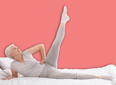 Morning fitness. Sporty senior lady doing fit exercises, lying on bed at home, free space