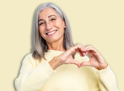 middle age gray hair woman smiling and feeling happy, cute, romantic and in love, making heart shape with both hands