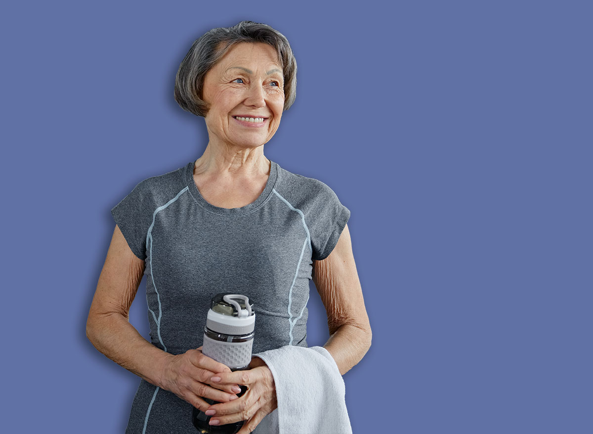 Senior woman displaying a happy smile holding a bottle of water in a gym
