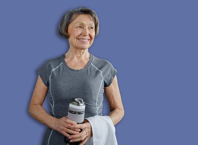 Senior woman displaying a happy smile holding a bottle of water in a gym