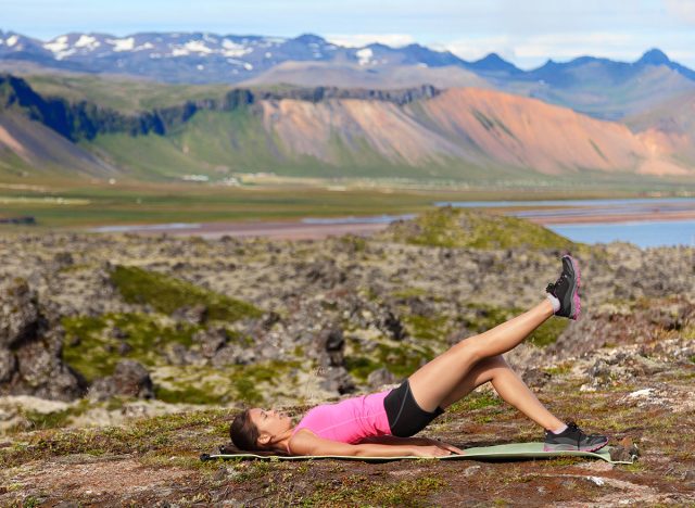 Fitness woman exercising single leg glute bridge exercise training butt and legs outside in beautiful nature landscape on Iceland. Fit female sports model working out.