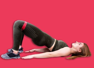 Young sportive woman doing a glute bridge using rubber resistance band isolated on gray background