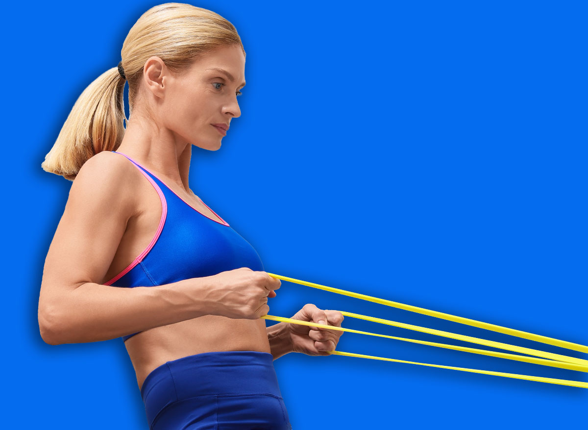 Fit woman doing exercise with fitness elastic band near laptop on mat at home