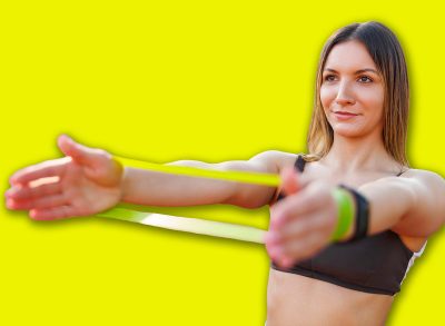 Active fit young woman in sports clothes doing an outdoor workout at basketball court, doing arm and chest exercises using resistance band