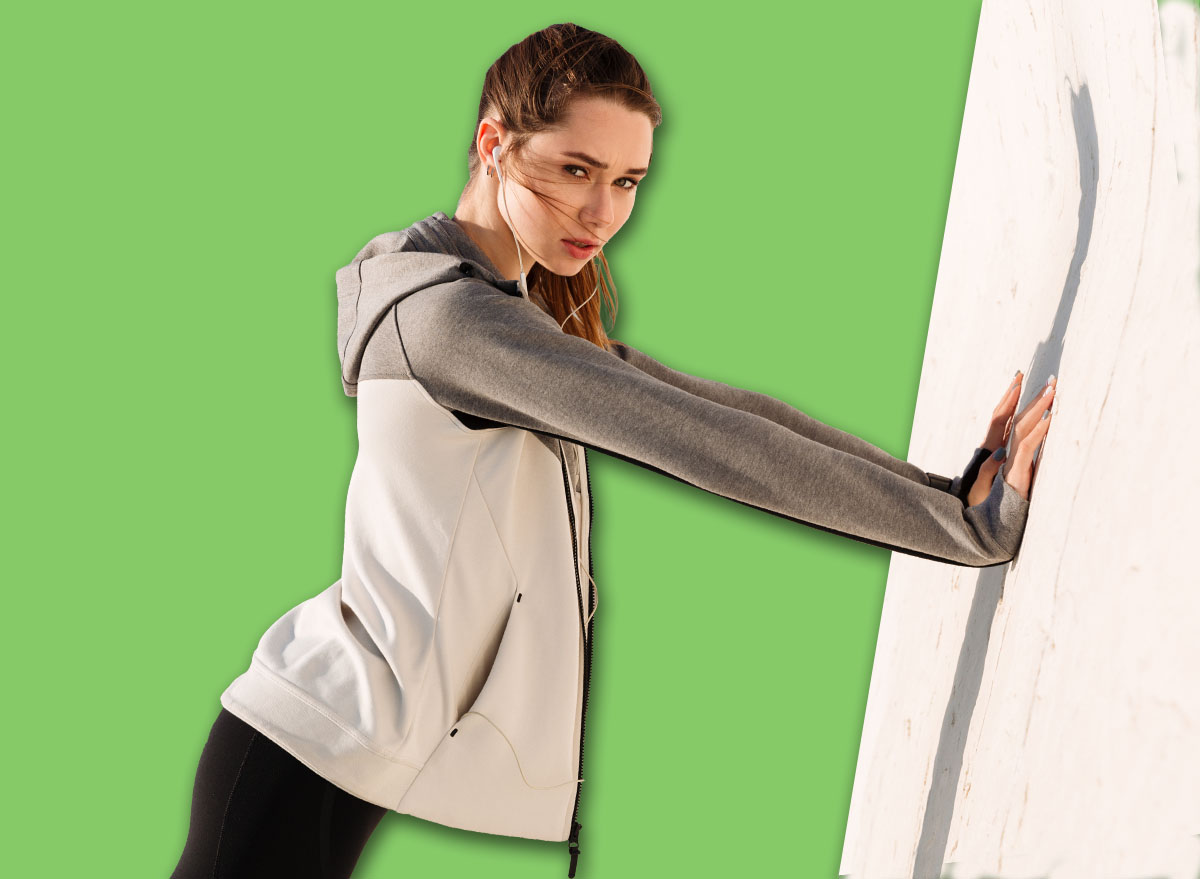 Photo of young slim sport woman doing push-ups while standing near white wall, looking at camera