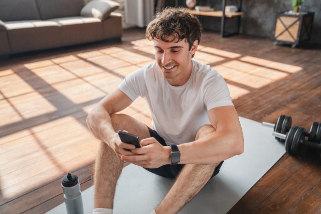 Athletic man using app on mobile phone during home workout
