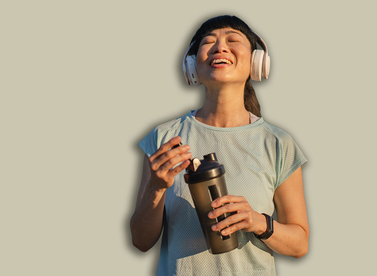 Mature japanese woman athlete wear headphones drink protein shake after jogging