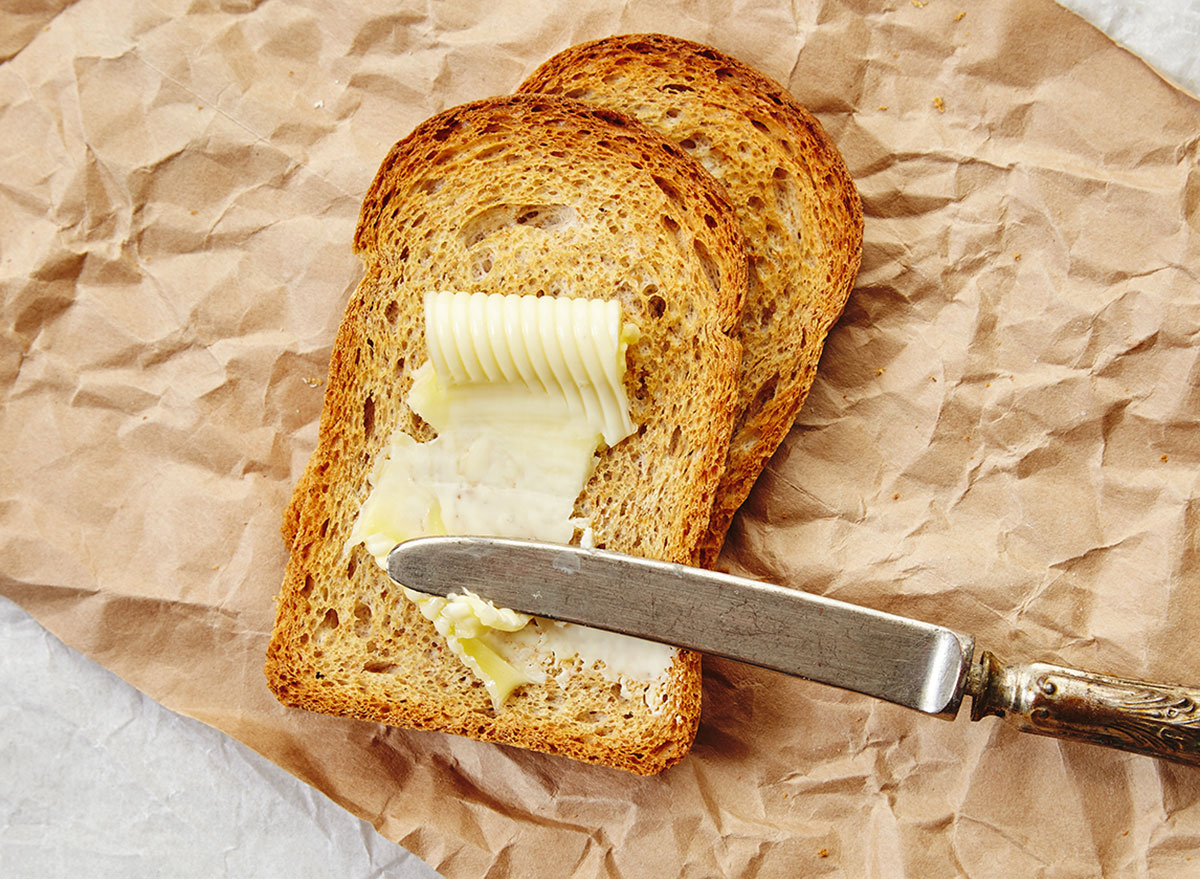 Top view of two slices of rye dry bread as toast with butter for breakfast with vintage knife on it. Everything on craft paper.