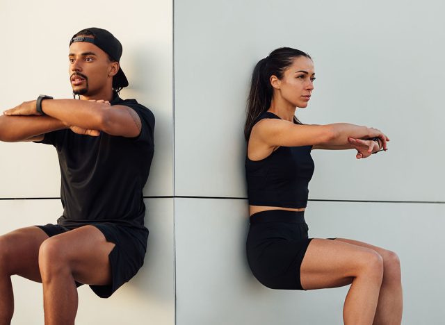 Fitness couple exercising together. Man and woman doing wall squat outdoors.
