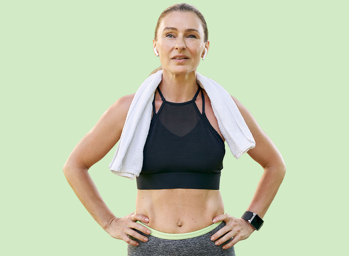 Stay fit. Attractive sporty woman in sportswear and wireless earphones looking away, standing with towel around her neck after workout in a green park on a sunny day