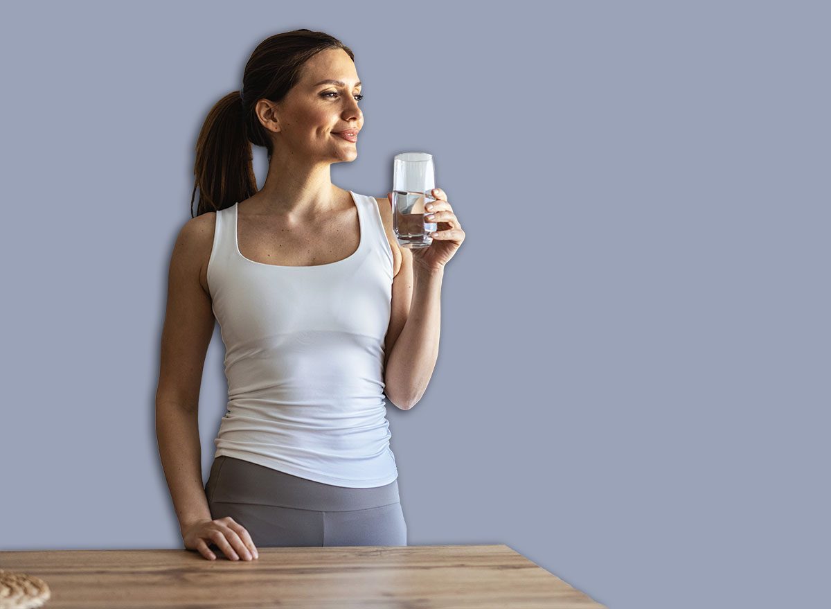 Caucasian beautiful woman in sportswear drink water after exercise at home. Young thirsty active sport girl takes a sips of clean mineral natural in cup after workout for health care in kitchen in house.