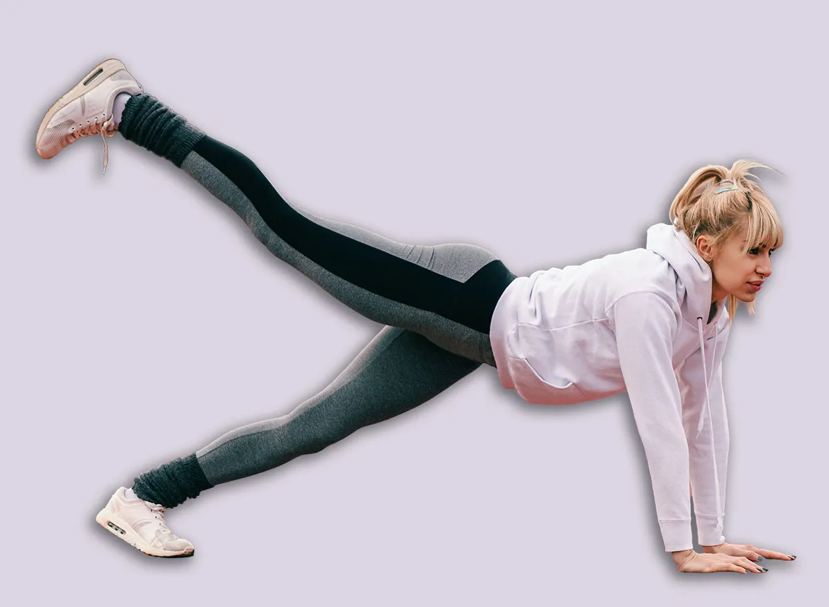 Beautiful Caucasian blonde woman doing plank leg raises on the racetrack before running. Full length, side view.