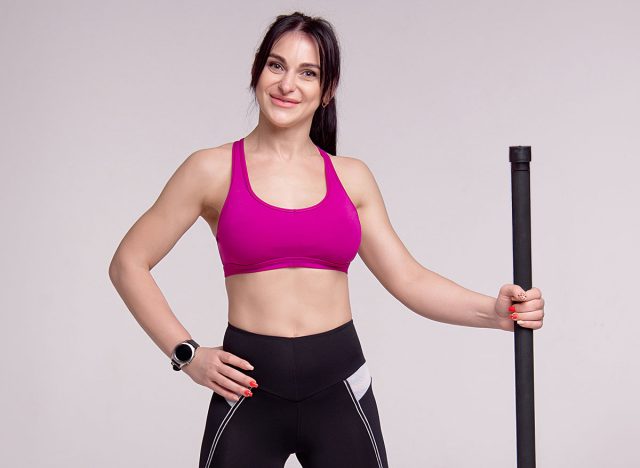 Beautiful muscular woman doing exercise with gymnastic stick on a gray background