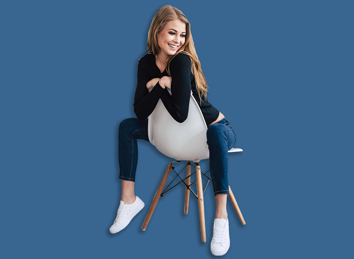 Take a look at this cutie! Beautiful young woman looking away with smile while sitting on chair against white background