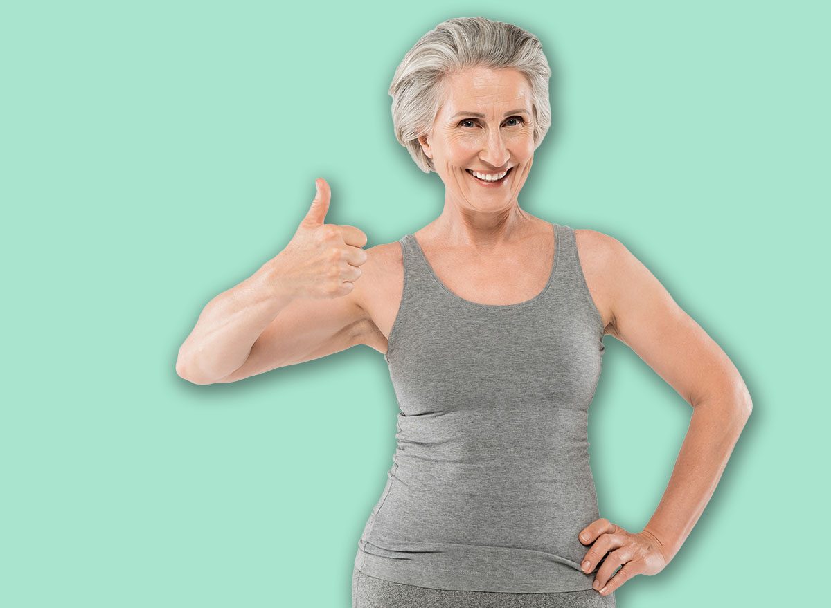cheerful and retired woman in sportswear posing with hand on hip and showing like isolated on grey, banner