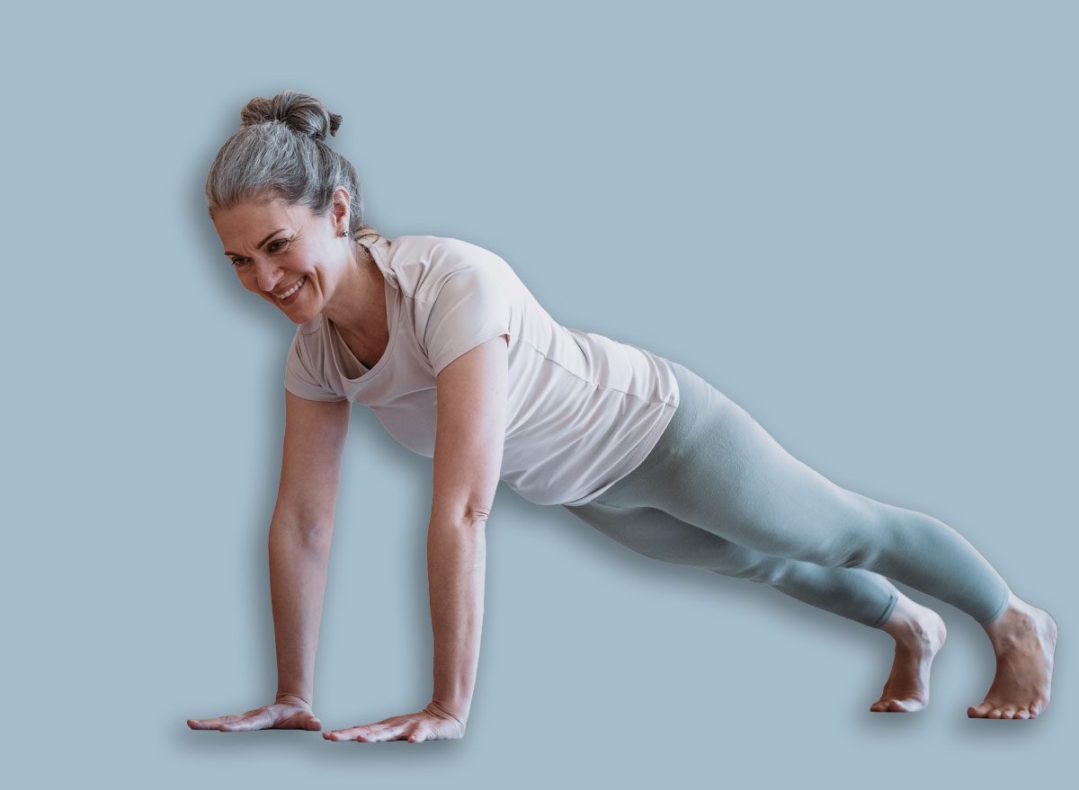 Positive sporty lady stretching in front of smartphone at home. Beautiful mature woman fitness blogger shooting video for her followers or having personal training online