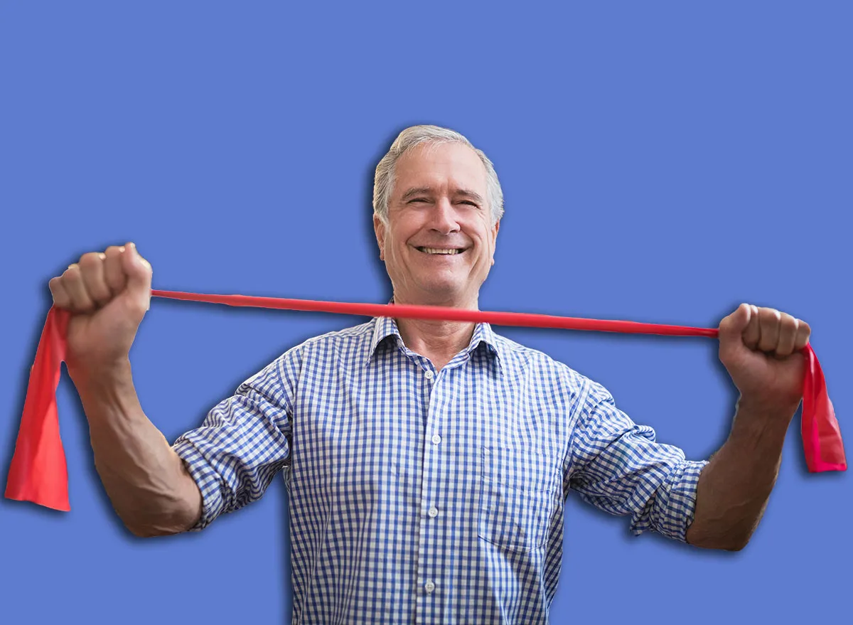 Portrait of smiling senior male patient pulling red elastic band at hospital ward