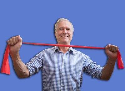 Portrait of smiling senior male patient pulling red elastic band at hospital ward