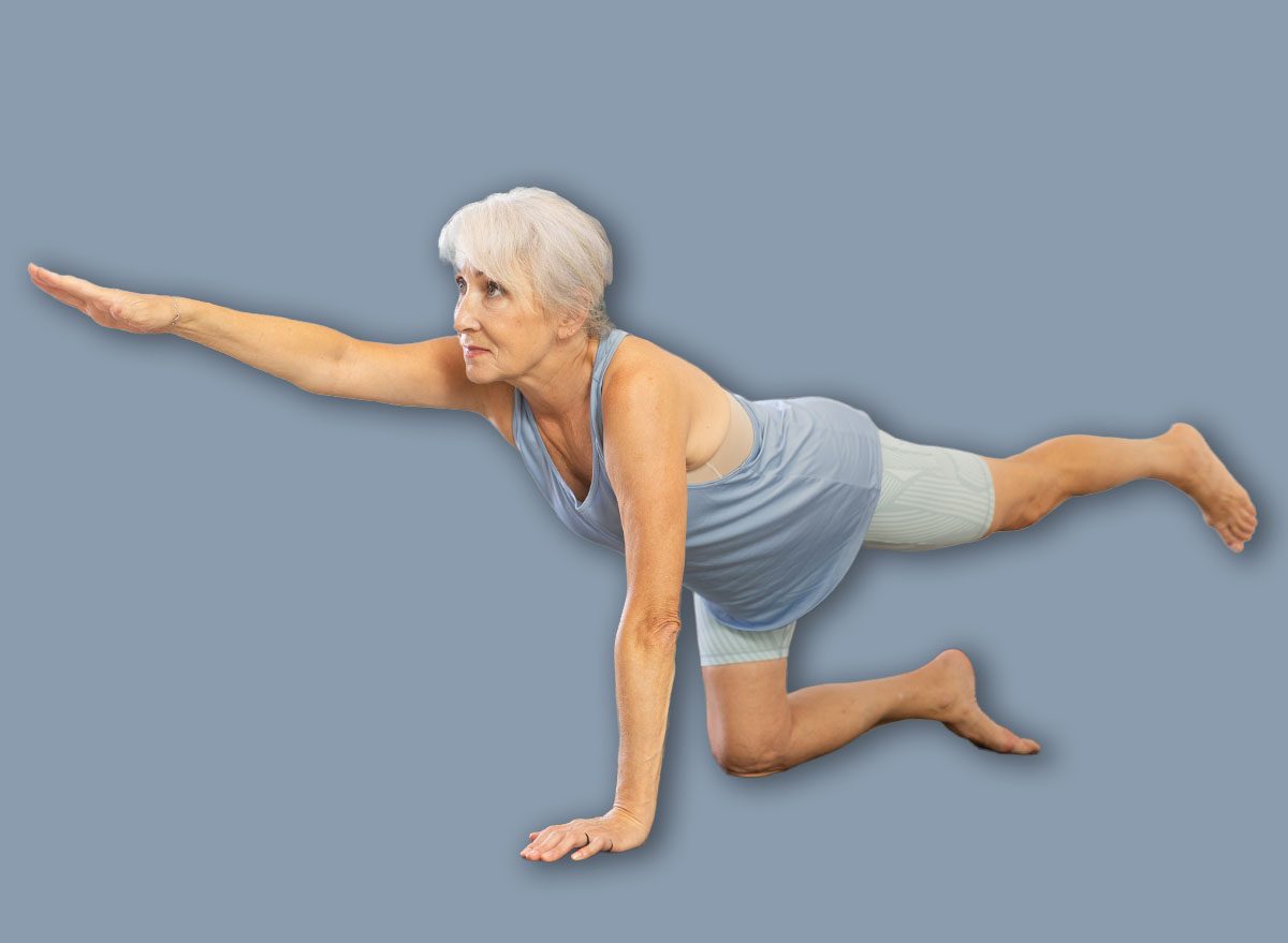Positive old woman practicing balancing table pose of yoga together with other attendees fitness classes