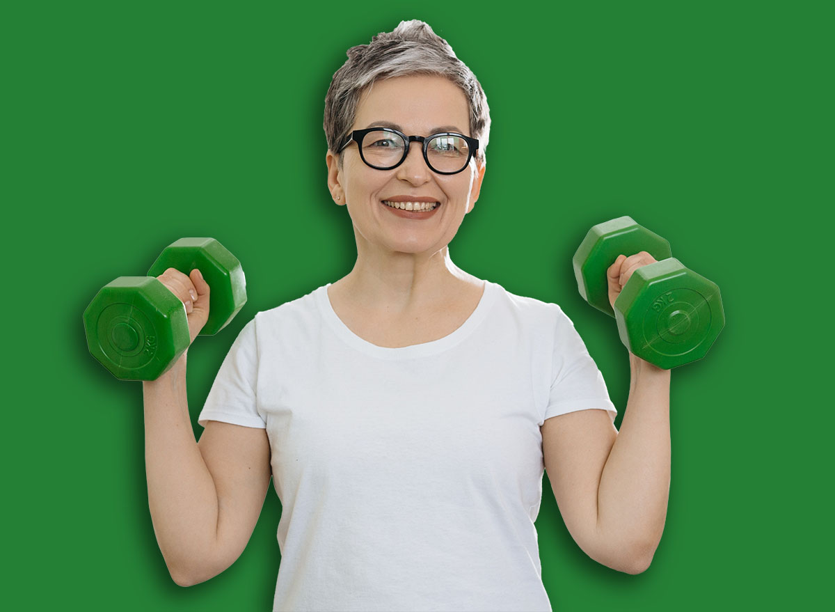Grey-haired woman smiling, holding dumbbells, exercising at home, promoting health and wellness. Active senior fitness