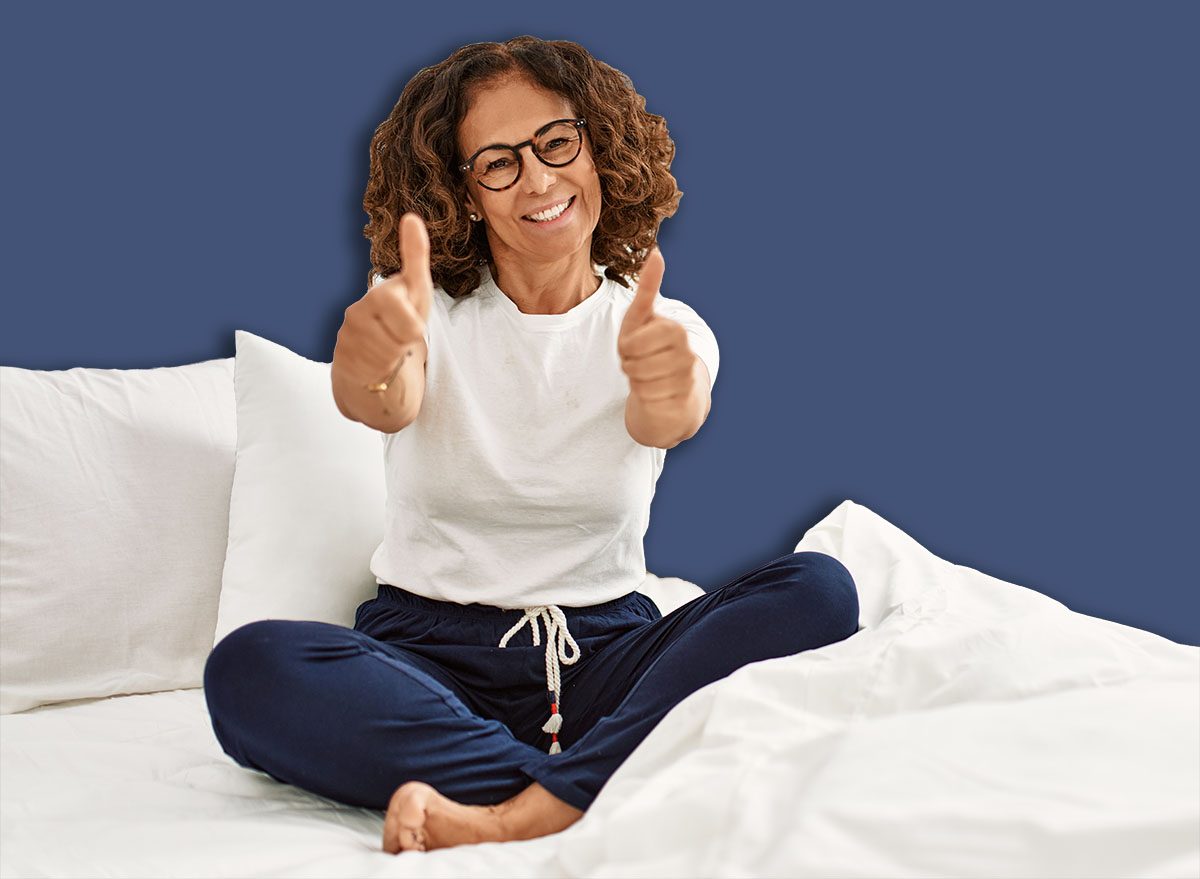 Middle age hispanic woman sitting on the bed at home approving doing positive gesture with hand, thumbs up smiling and happy for success. winner gesture.