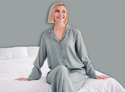 Photo of slumber happy girl wearing grey pajama looking curious in window sitting bedroom white cozy blanket and pillows isolated indoors