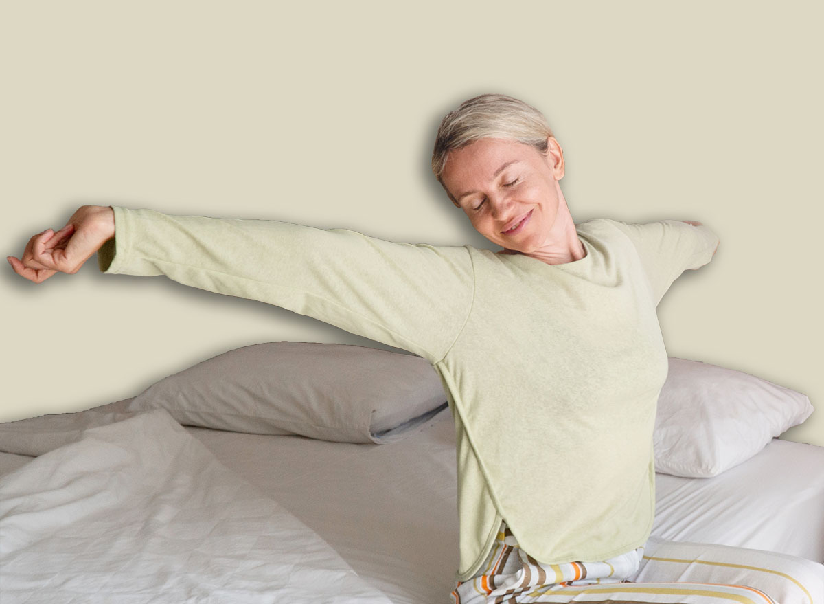 Smiling Woman Stretching arms after sleep in bed at bedroom. Enjoying middle age woman with open arms in freedom