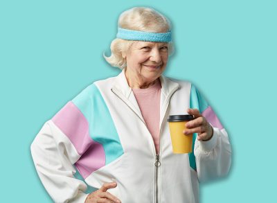 Mature female jogger in white sports suit taking a rest after morning running, holding cold drink in hands and looking at camera with cheerful look, isolated over blue background.