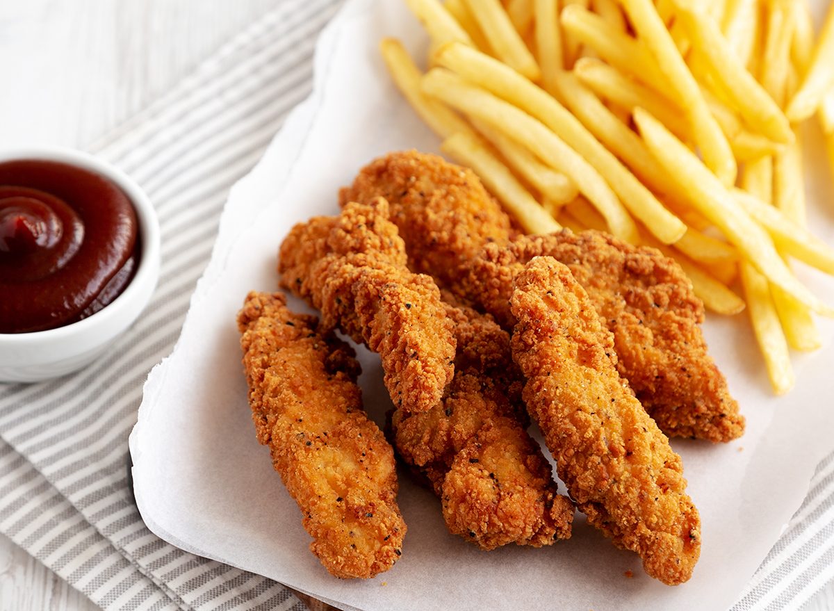 Homemade Chicken Tenders with French Fries and BBQ Sauce on a rustic wooden board, side view.