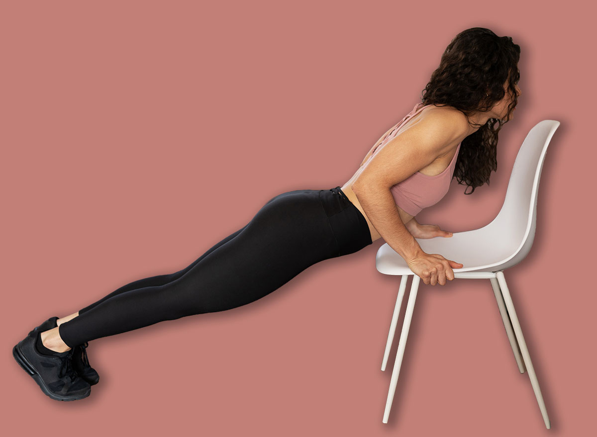 Side view of an active young woman wearing sportswear doing push ups with the help of a chair at home