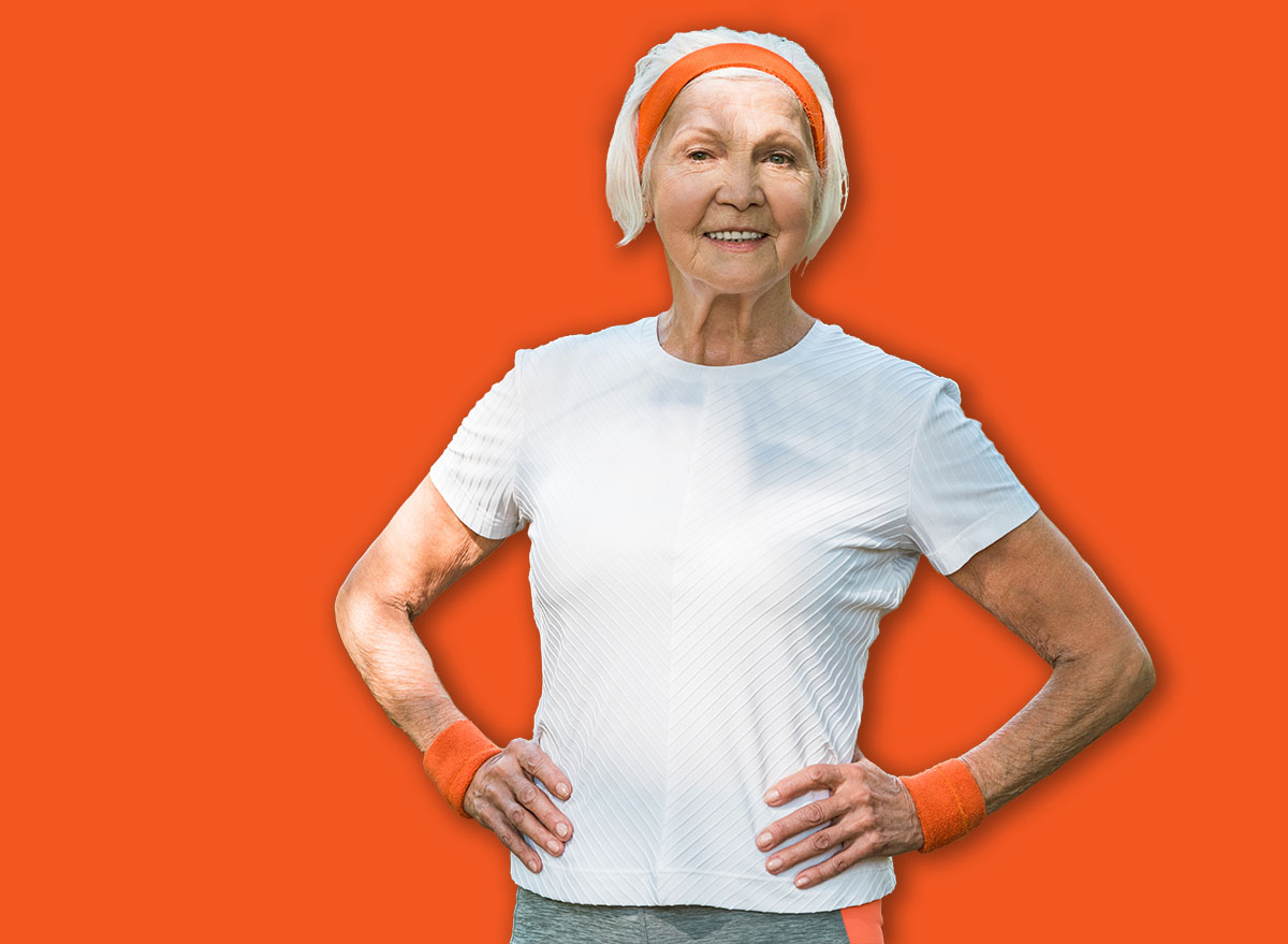 selective focus of cheerful senior woman standing with hands on hips near multicultural pensioners in park