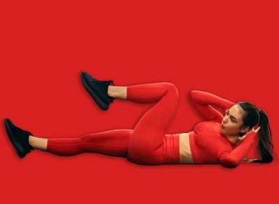 A fit sportswoman is doing bicycle crunches on a gym floor.