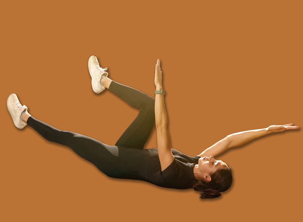 Woman doing dead bug core exercise on mat beside laptop at home. Concept of online fitness classes, abdominal strength, posture support, coordination training and effective home workout routines.